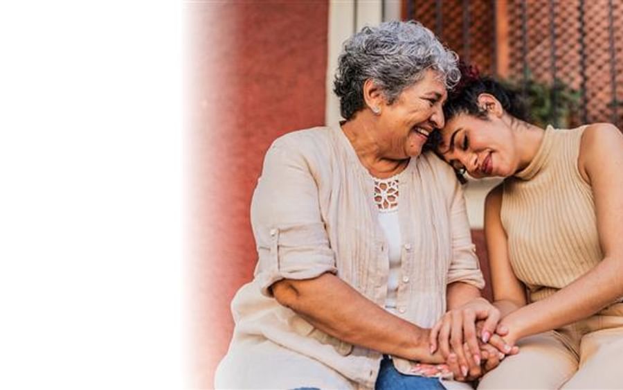 Two people outdoors, smiling and holding hands, one leaning on the other's shoulder.