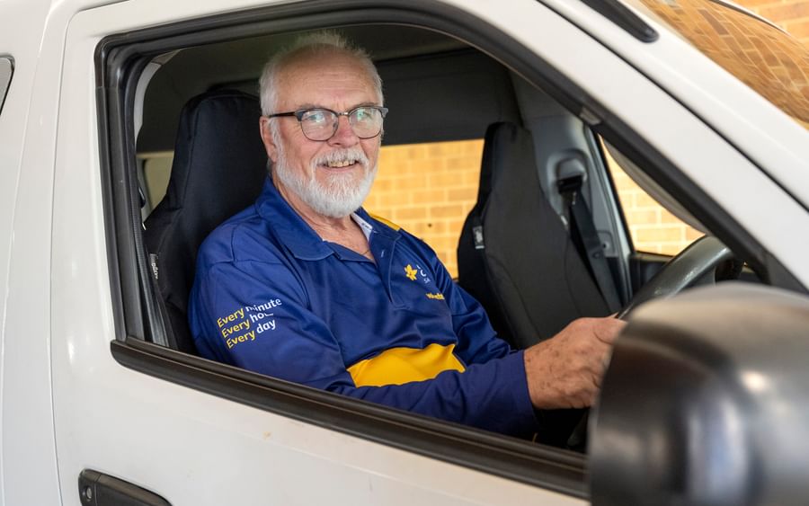 Person in drivers seat of van holding the steering wheel while looking at the camera.