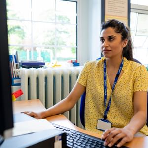 Person at a desk using a computer in a bright office, wearing a yellow floral shirt and blue lanyard.