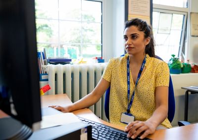 Person at a desk using a computer in a bright office, wearing a yellow floral shirt and blue lanyard.