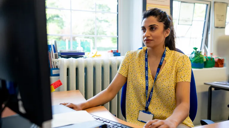 Person at a desk using a computer in a bright office, wearing a yellow floral shirt and blue lanyard.
