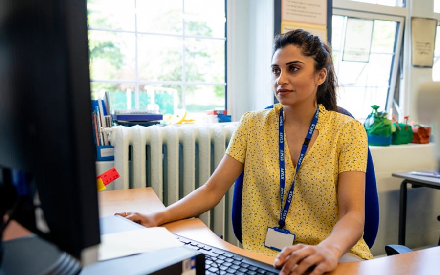 Person at a desk using a computer in a bright office, wearing a yellow floral shirt and blue lanyard.