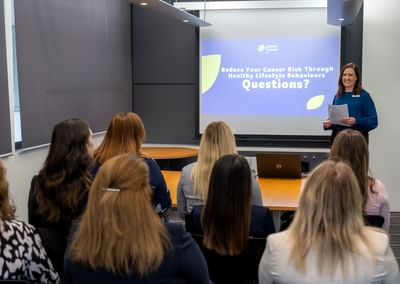 Speaker presenting to a seated audience; projected slide about cancer risk and lifestyle.