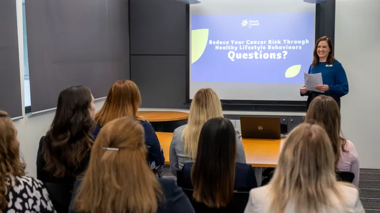 Speaker presenting to a seated audience; projected slide about cancer risk and lifestyle.