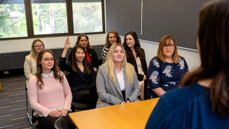 Group of people seated in a conference room listening to a speaker at a wooden table.