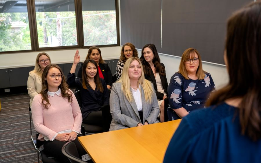 Group of people seated in a conference room listening to a speaker at a wooden table.