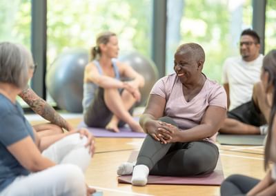 Diverse group in a yoga class sits on mats, smiling and chatting.