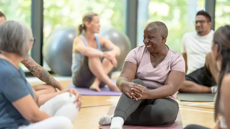 Diverse group in a yoga class sits on mats, smiling and chatting.