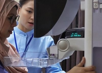 Person wearing hijab and a clinician operate a medical device with a clear tray.