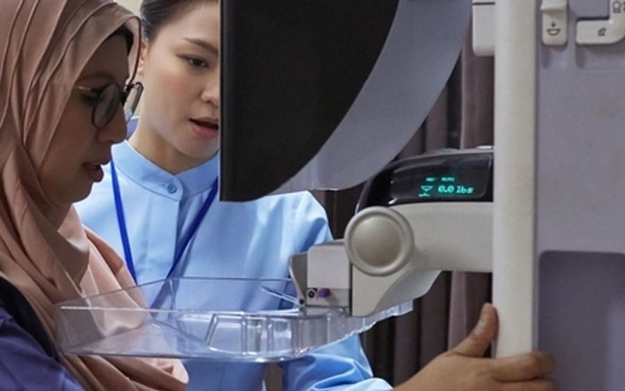 Person wearing hijab and a clinician operate a medical device with a clear tray.