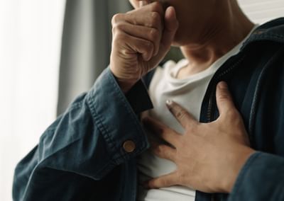 Person in a blue denim jacket covers their mouth with one hand, the other resting on their chest.