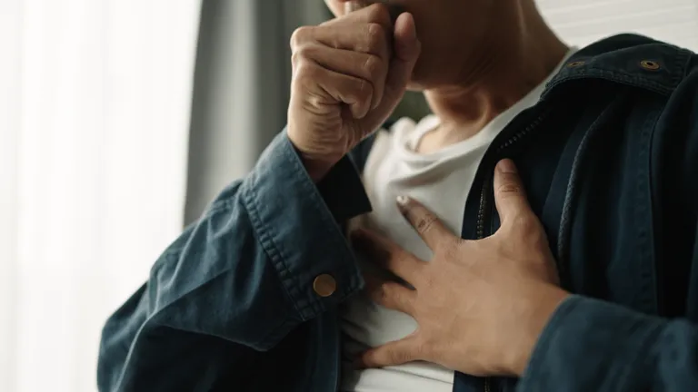 Person in a blue denim jacket covers their mouth with one hand, the other resting on their chest.