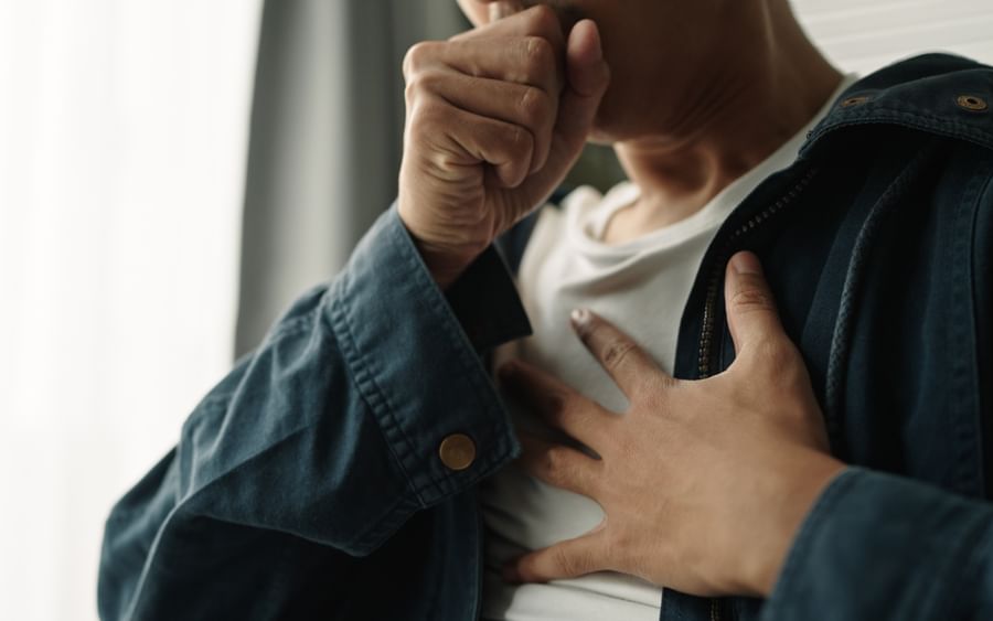 Person in a blue denim jacket covers their mouth with one hand, the other resting on their chest.