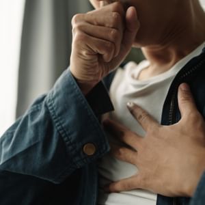 Person in a blue denim jacket covers their mouth with one hand, the other resting on their chest.