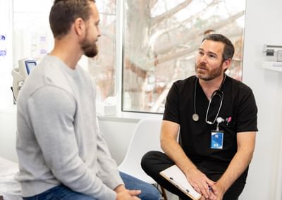 Medical consultation in a clinic with a doctor in black scrubs and stethoscope talking to a patient.