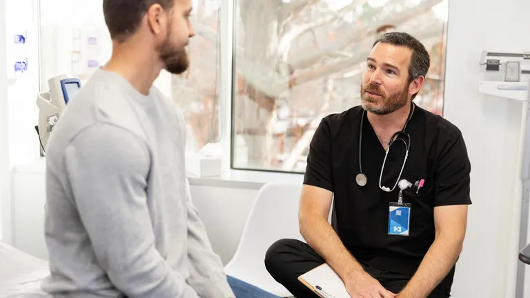 Medical consultation in a clinic with a doctor in black scrubs and stethoscope talking to a patient.