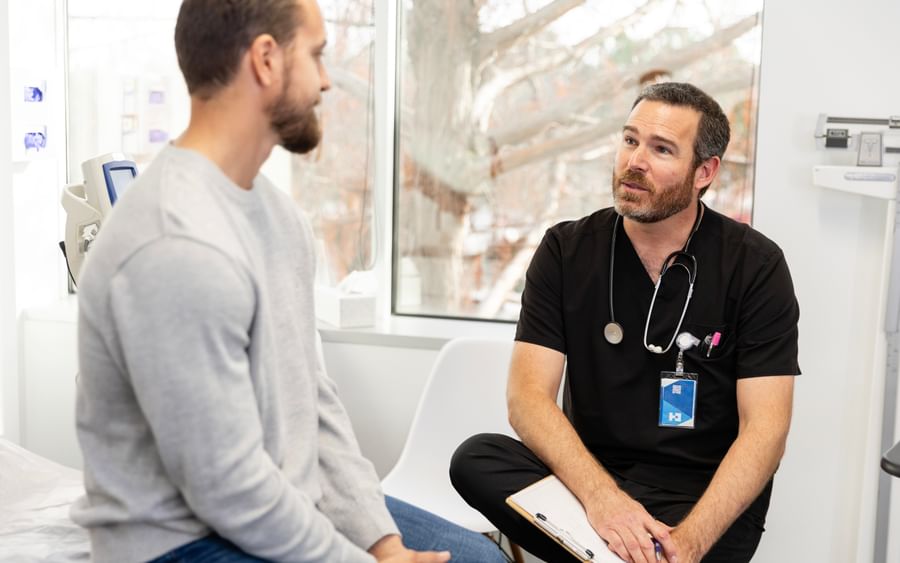 Medical consultation in a clinic with a doctor in black scrubs and stethoscope talking to a patient.