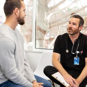 Medical consultation in a clinic with a doctor in black scrubs and stethoscope talking to a patient.