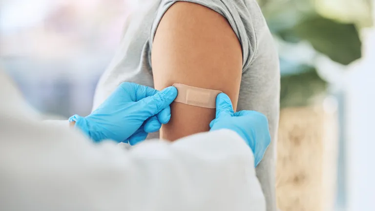 Close-up of a person’s upper arm as a clinician wearing blue gloves applies a bandage.