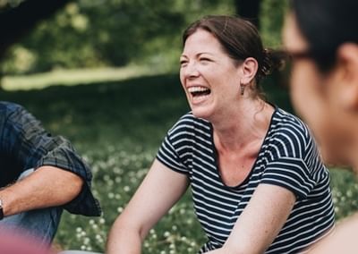 A group of people laughing together outdoors in a sunny park.
