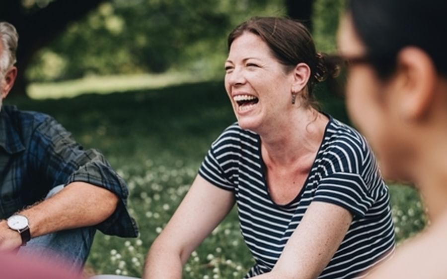 A group of people laughing together outdoors in a sunny park.