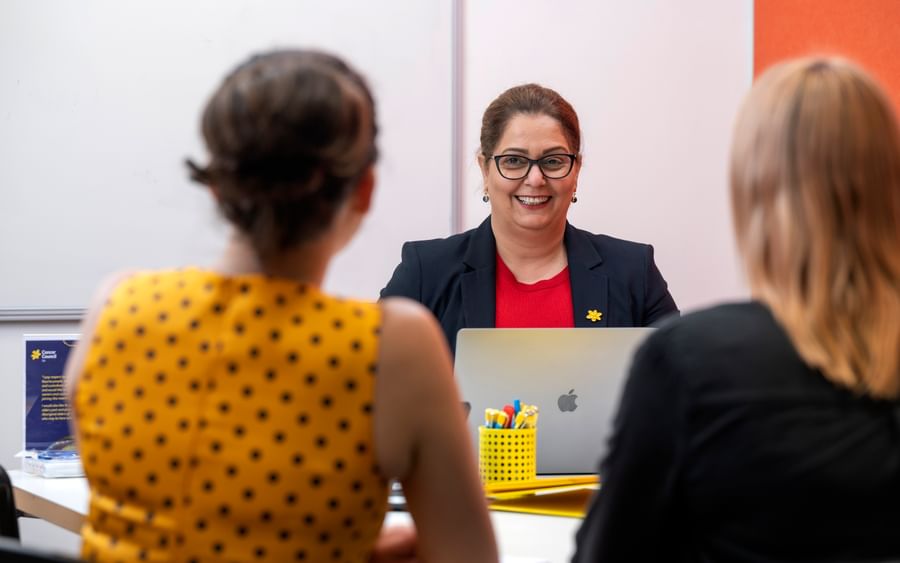 Smiling person in a navy blazer and red top leads a meeting with two colleagues.