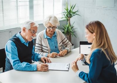 Three people sit around a white table in a bright office, reviewing papers with a laptop.