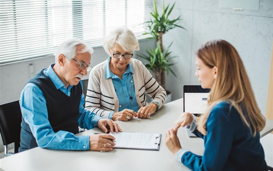 Three people sit around a white table in a bright office, reviewing papers with a laptop.