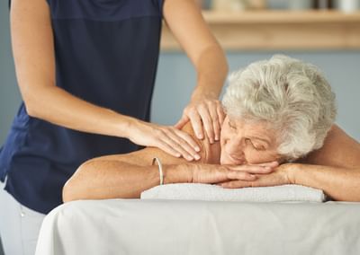 A therapist gives an elderly person a back massage on a treatment table.