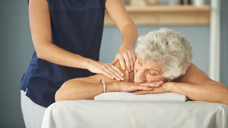 A therapist gives an elderly person a back massage on a treatment table.