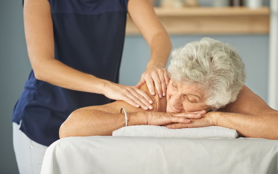 A therapist gives an elderly person a back massage on a treatment table.