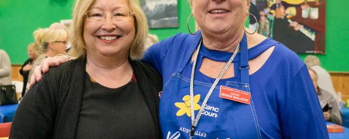 Two people smiling and posing together at a community event, indoors with green walls and balloons.