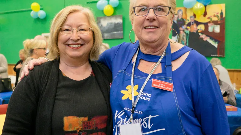 Two people smiling and posing together at a community event, indoors with green walls and balloons.