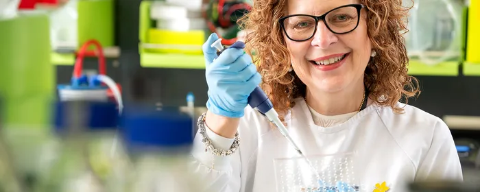 Lab worker with curly hair and glasses, in a white coat, using a pipette in a bright lab.