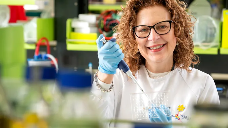 Lab worker with curly hair and glasses, in a white coat, using a pipette in a bright lab.