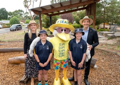 Two adults and two kids posing with a yellow seagull mascot wearing a hat in a park.