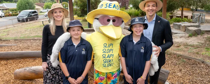 Two adults and two kids posing with a yellow seagull mascot wearing a hat in a park.