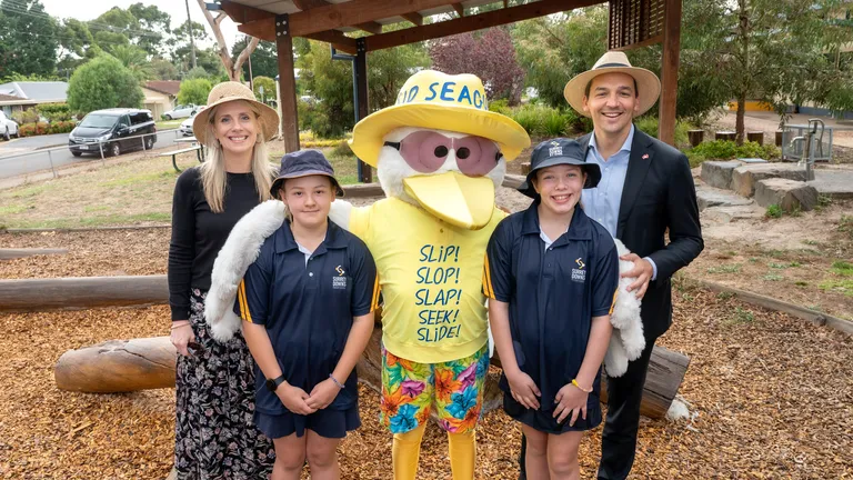 Two adults and two kids posing with a yellow seagull mascot wearing a hat in a park.