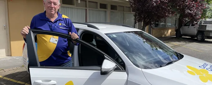 Person in blue and yellow polo by white Cancer Council SA car, purple-leaved tree in background.