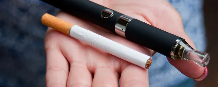 A hand holding a black vape pen with a cigarette resting on the palm.