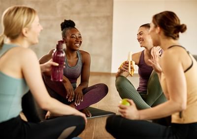 Four people in athletic wear sit on yoga mats, smiling and chatting during a fitness break.