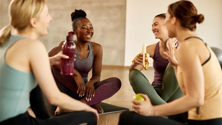 Four people in athletic wear sit on yoga mats, smiling and chatting during a fitness break.