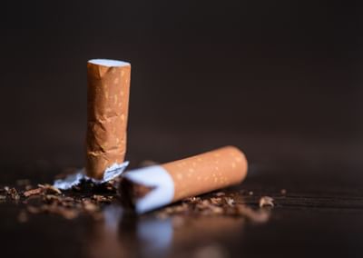 Two broken cigarettes on a dark wooden surface with scattered tobacco flakes.