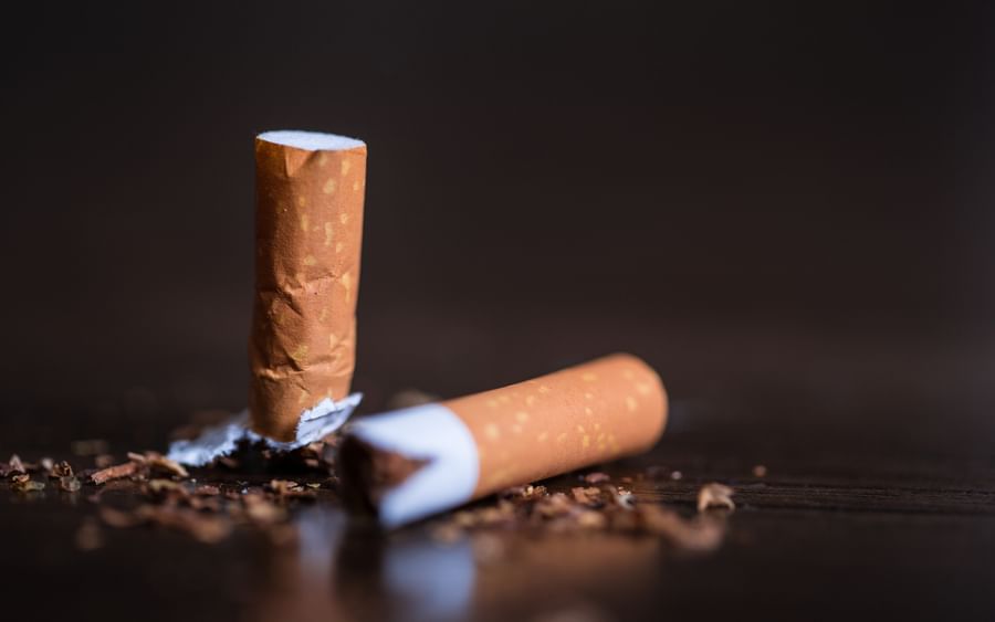 Two broken cigarettes on a dark wooden surface with scattered tobacco flakes.