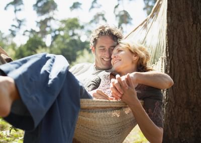 A couple relaxing in a hammock outdoors on a sunny day, smiling.