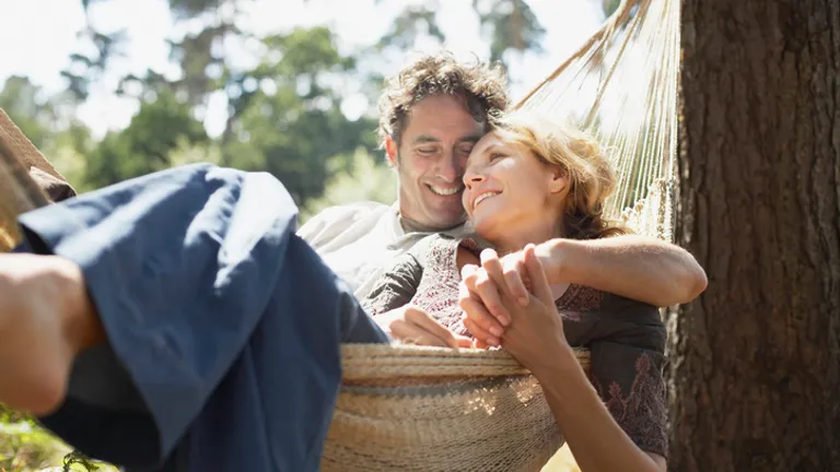 A couple relaxing in a hammock outdoors on a sunny day, smiling.