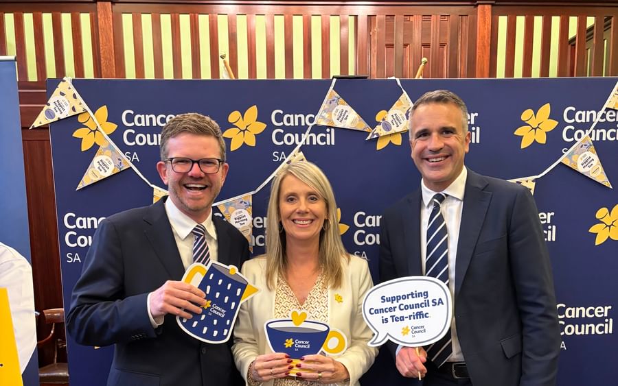 Three people in formal attire pose at a blue Cancer Council SA backdrop, holding props.