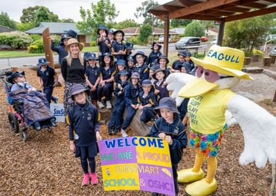 Group of students in navy uniforms with a sun-smart mascot and a welcome sign.