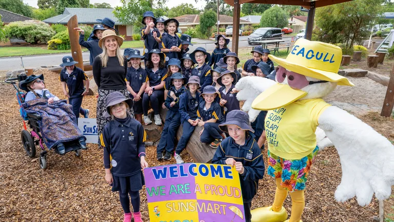 Group of students in navy uniforms with a sun-smart mascot and a welcome sign.