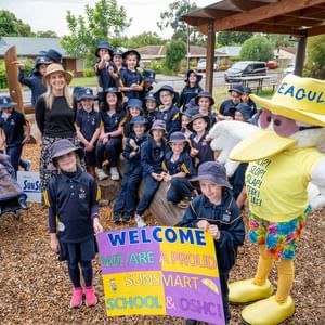 Group of students in navy uniforms with a sun-smart mascot and a welcome sign.